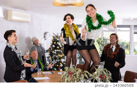 Excited young women with New Year tinsels on table during corporate party with champagne in meeting room Excited young women with New Year tinsels on table during corporate party with champagne in meeting room 143360508