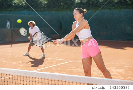 Padel tennis couple in court playing double match. Young beautiful woman in white t-shirt hits tennis ball with racket Padel tennis couple in court playing double match. Young beautiful woman in white t-shirt hits tennis ball with racket 143360582