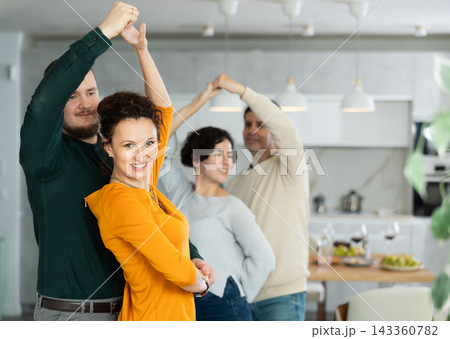 Friends dancing. Cheerful young people dancing and drinking while enjoying home party on room 143360782