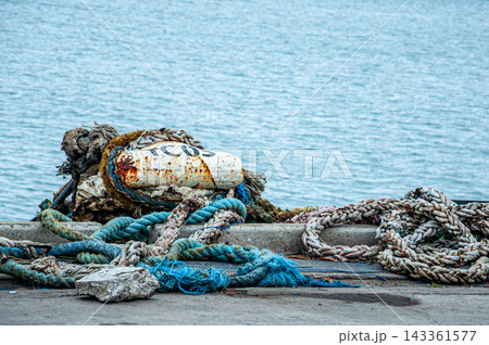 Worn mooring ropes and rusty buoy on a harbor pier Worn mooring ropes and rusty buoy on a harbor pier 143361577