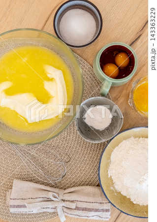 Baking ingredients. Home recipe. Liquid yellow butter raw eggs flour sugar ingredient measured in ceramic bowls on wooden table background. 143363229
