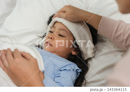 mother applying cold compress on sick daughter's forehead in bed 143364115