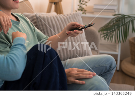 Young couple relaxing on sofa holding remote control while watching television together at home 143365249
