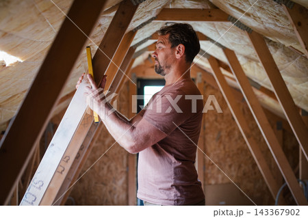 Homeowner doing DIY renovation work in unfinished attic. Homeowner doing DIY renovation work in unfinished attic. 143367902