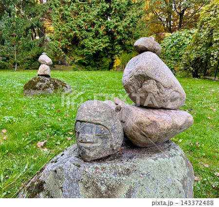 Stone balance and equilibrium concept on a green grass lawn with an ancient looking carved stone head face sculpture in a public park. 143372488