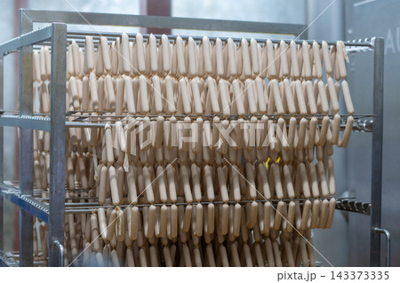 Rows of Fresh Sausages Hanging on Racks in Food Processing Factory Rows of Fresh Sausages Hanging on Racks in Food Processing Factory 143373335