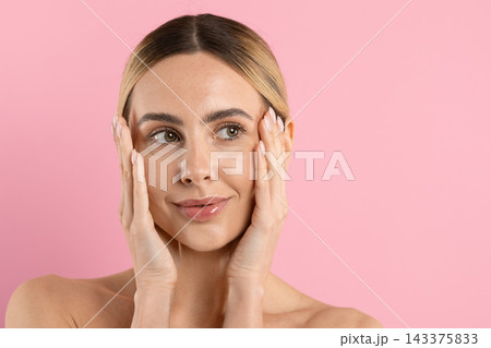 Young woman with hands on her cheeks, looking aside on pink background Young woman with hands on her cheeks, looking aside on pink background 143375833