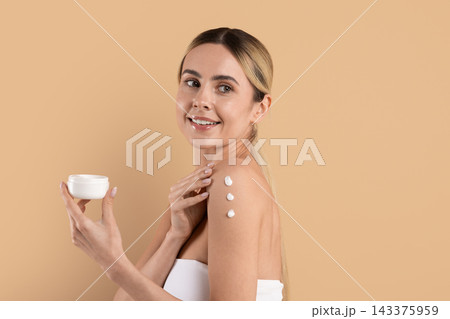 Young woman holding cosmetic cream jar and applying moisturizer to her shoulder Young woman holding cosmetic cream jar and applying moisturizer to her shoulder 143375959