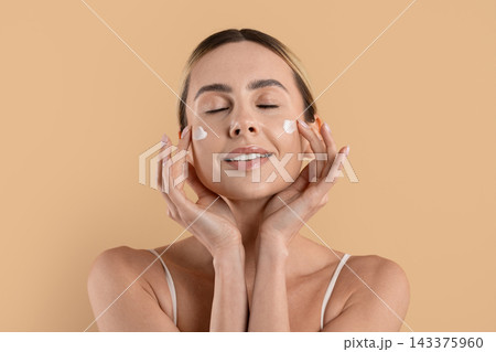 Woman with eyes closed gently applying moisturizing face cream on both cheeks Woman with eyes closed gently applying moisturizing face cream on both cheeks 143375960