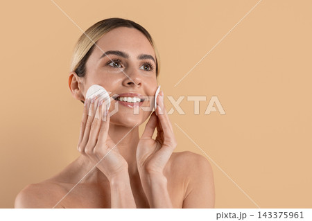 Young woman cleansing face with cotton pads against beige studio background Young woman cleansing face with cotton pads against beige studio background 143375961