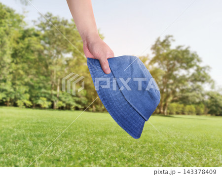 Man holding blue bucket hat on green grass background. 143378409