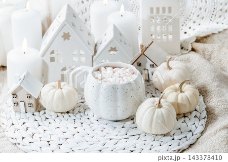 autumn background. Cozy Autumn Hot Chocolate with Mini Pumpkins and Fall Decor Warm mug of hot chocolate with mini marshmallows, white pumpkins and home decor. Inviting autumn scene 143378410