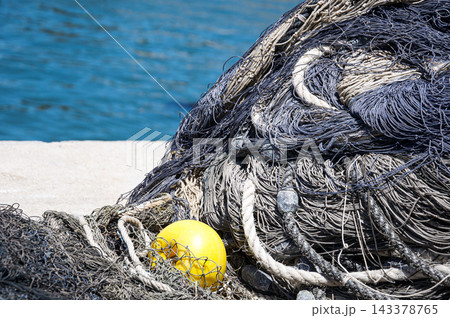 Pile of commercial fishing nets and yellow float on concrete pier 143378765
