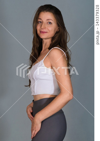 Confident female Pilates instructor in a relaxed professional pose, standing side-on in white sportswear 143379328