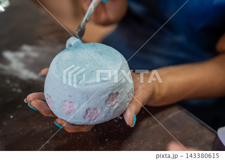 Hands applying glaze to outer surface of handmade ceramic mug with brush. Close up pottery glazing process represents craftsmanship and handmade ceramic production Hands applying glaze to outer surface of handmade ceramic mug with brush. Close up pottery glazing process represents craftsmanship and handmade ceramic production 143380615