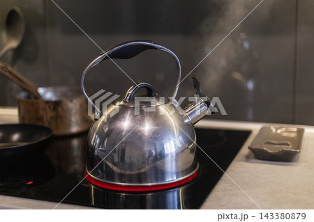 Stainless steel kettle on black induction cooktop Stainless steel kettle on black induction cooktop 143380879
