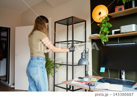 Woman placing new shelf beside desk in home office Woman placing new shelf beside desk in home office 143380887