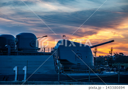 Naval artillery guns and armaments on a military warship at sunset 143380894