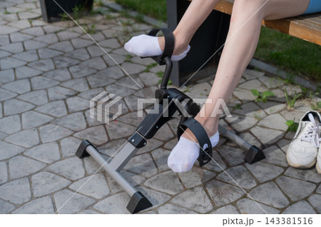 A woman uses Pedal Exercise Machine for self-rehabilitation outdoors. Close-up of feet.  143381516