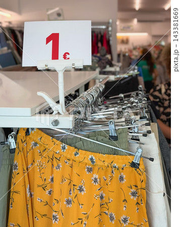 Closeup of clear 1 euro price sign inside thrift store and second hand clothes on hangers. Affordable used fashion, reuse, budget shopping. Sustainability, circular economy, zero waste, thrift concept 143381669