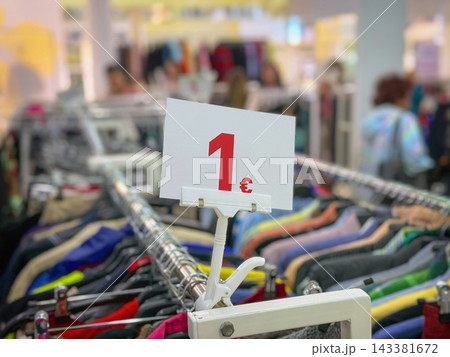 Close view of 1 euro price sign above racks of second hand clothes in thrift store. Sustainability, circular economy, zero waste, thrift clothing, reuse and overconsumption concept Close view of 1 euro price sign above racks of second hand clothes in thrift store. Sustainability, circular economy, zero waste, thrift clothing, reuse and overconsumption concept 143381672
