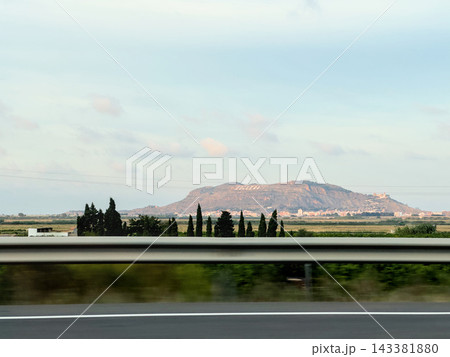 Cullera mountain and town behind cypress trees and rice fields, view from highway Cullera mountain and town behind cypress trees and rice fields, view from highway 143381880