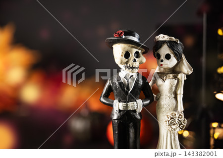 Skeleton bride and groom figurines beside glowing haunted house, pumpkins and smoke. Gothic Halloween wedding decorations on dark background with ample copy space. Halloween holiday card. 143382001