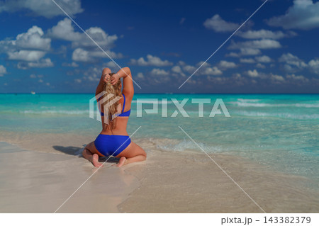 Woman in blue swimsuit sitting on beach shore Woman in blue swimsuit sitting on beach shore 143382379