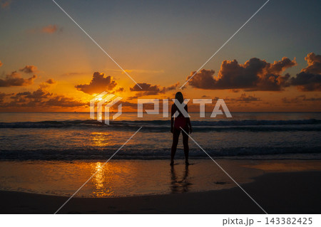 Silhouette of woman standing on shore during ocean sunset Silhouette of woman standing on shore during ocean sunset 143382425