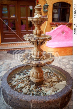 Tiered stone fountain with seashells and pebbles in colorful courtyard Tiered stone fountain with seashells and pebbles in colorful courtyard 143382433