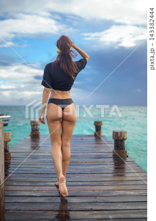 Woman in black swimwear walking on wet wooden pier by turquoise sea Woman in black swimwear walking on wet wooden pier by turquoise sea 143382444