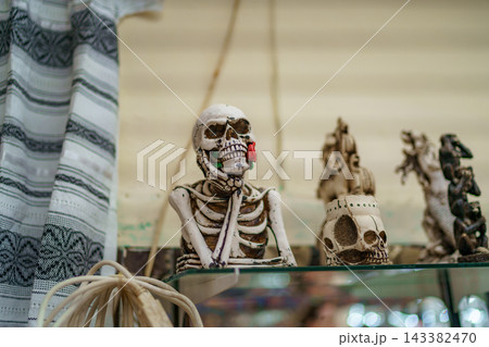Skeleton figurine resting chin on hand with red rose in mouth 143382470