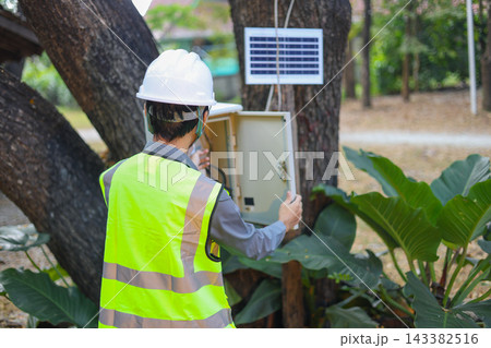 Technician working on an outdoor electrical system powered by a solar panel. Technician working on an outdoor electrical system powered by a solar panel. 143382516
