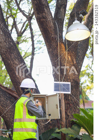 Technician working on an outdoor electrical system powered by a solar panel. Technician working on an outdoor electrical system powered by a solar panel. 143382519