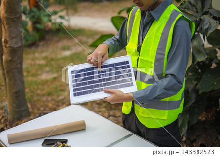 A person in safety gear holding a portable solar panel working outdoor A person in safety gear holding a portable solar panel working outdoor 143382523