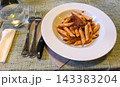 ミートソースのペンネパスタとフォークとナイフが並ぶ食卓 143383204