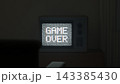 3D render of a vintage television in a dark room showing pixel Game Over text over static noise with chromatic aberration glitch, retro gaming concept. 143385430