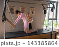 A woman in activewear does pilates exercises for the chest and back muscles Pilates Cadillac in a sunlite studio, Trapeze Table workout machine 143385864