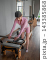 Young caucasian women exercising Scooter on pilates reformers for the hips and glutes in a bright studio. Her workout focuses on strength and flexibility 143385868