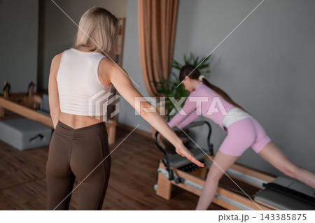 Young caucasian women exercising Scooter on pilates reformers for the hips and glutes in a bright studio. Her workout focuses on strength and flexibility 143385875
