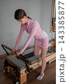 Young caucasian women exercising Scooter on pilates reformers for the hips and glutes in a bright studio. Her workout focuses on strength and flexibility 143385877