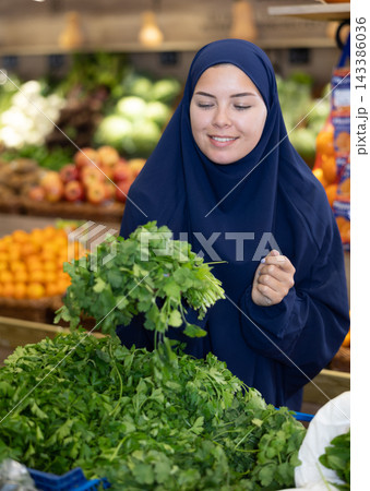 Delighted young Muslim woman purchaser choosing cilantro in grocery store Delighted young Muslim woman purchaser choosing cilantro in grocery store 143386036