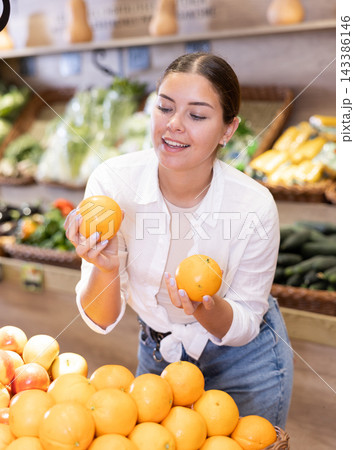 Happy smiling woman making purchases in supermarket, choosing fresh oranges Happy smiling woman making purchases in supermarket, choosing fresh oranges 143386146