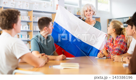 Interesting story about Russia while teaching high school students in school library. Teacher holds flag of Russia in her hands Interesting story about Russia while teaching high school students in school library. Teacher holds flag of Russia in her hands 143386196