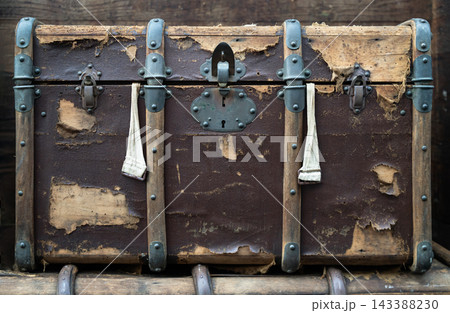 A rustic, heavily weathered antique travel trunk showcases a story of bygone journeys with its peeling leather exterior and dark wooden framing. Reinforced with sturdy metal latches, decorative studs, A rustic, heavily weathered antique travel trunk showcases a story of bygone journeys with its peeling leather exterior and dark wooden framing. Reinforced with sturdy metal latches, decorative studs, 143388230