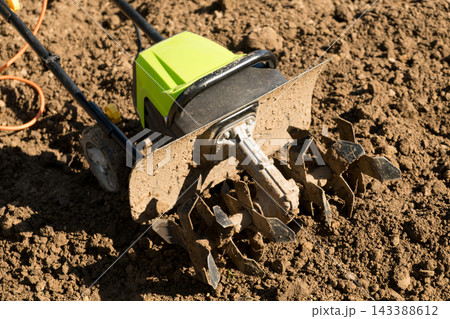 Amidst vibrant greenery, a garden tiller effectively aerates and prepares the soil for crop planting. Amidst vibrant greenery, a garden tiller effectively aerates and prepares the soil for crop planting. 143388612
