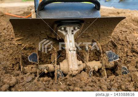 The sharp blades of a tiller are actively working through dark, moist soil, ensuring optimal conditions for vegetable planting. 143388616