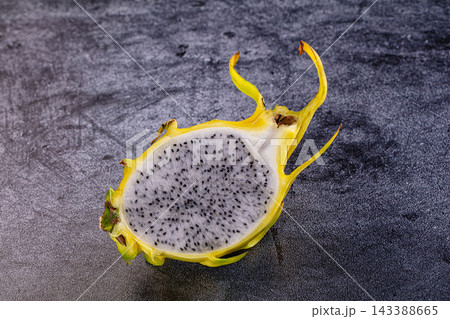 Halved yellow dragon fruit with white flesh and black seeds on dark textured stone surface tropical fruit 143388665