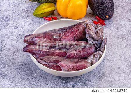 Gray textured surface with fresh purple squid in white bowl surrounded by yellow bell pepper starfruit avocado and red chili peppers seafood preparation Gray textured surface with fresh purple squid in white bowl surrounded by yellow bell pepper starfruit avocado and red chili peppers seafood preparation 143388712