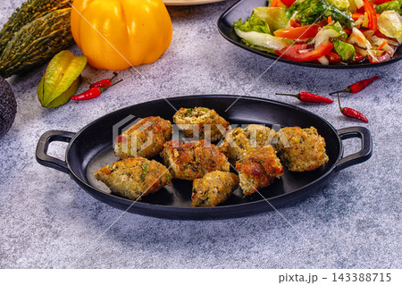 Grey stone table with roasted minced chicken kebab pieces in black oval dish, yellow pepper, chillies, bitter melon and fresh vegetable salad, healthy homemade food 143388715